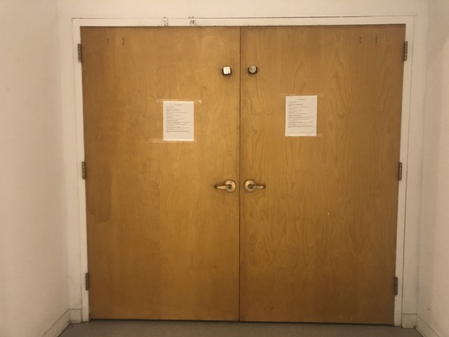 Two 8.5-inch by 11-inch pieces of paper are taped to wooden double doors. Printed on the paper in capital letters reads the following text: NOTICE OF DEEMED CONSENT YOU ARE ENTERING THE PREMISES. BY ENTERING THE PREMISES, YOU HEREBY CONSENT TO THE OBSTRUC