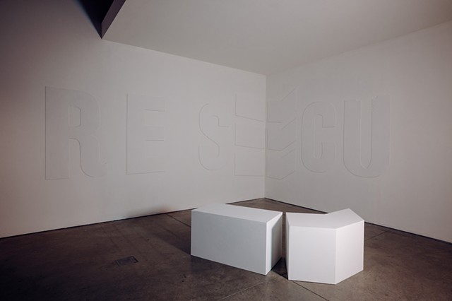 “Rescue,” a plaster wall relief, and two geometric forms are positioned on the gallery floor.   The five-foot-high white plaster relief 1/8th inch thick sits on the left gallery wall and spills into the alcove, bending around the back left corner. Because