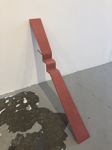 A rosy-red inclined structure is interrupted by a stepped midsection and secured by steel rod into a wall. 