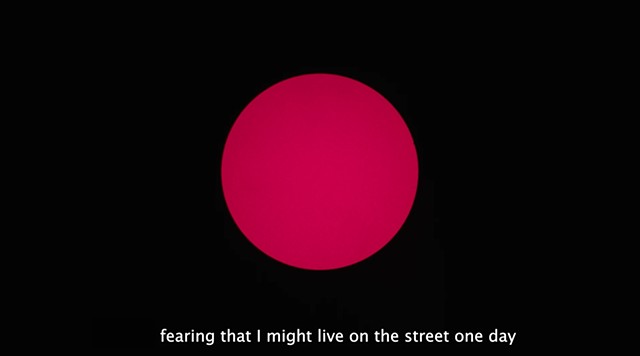 A large red circle on a black background with the caption red in the lower thirds of the screen. This is a still from a video piece titled 'Tell Me' (2016) 