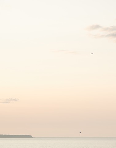 A color photograph depicts a pastel sunset over the bay of Green Bay in Door County, Wisconsin, with an island on the horizon.