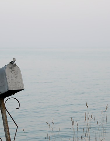 A color photograph depicts a metal mailbox and grasses near the edge of Lake Michigan in Door County, Wisconsin.